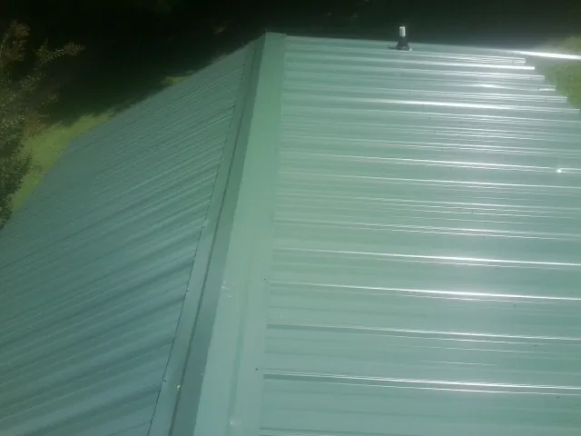 New green metal panels meeting at the ridge of a roof — Flat Roof Repair work by our crew in Goshen